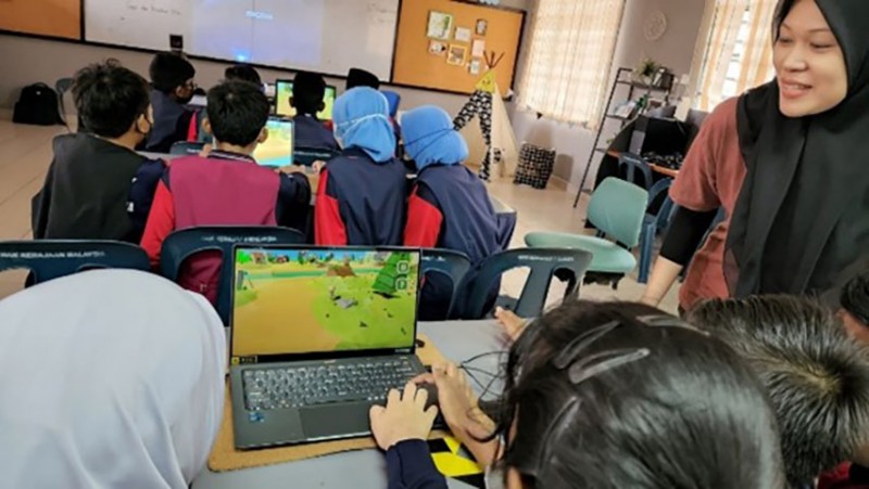 Over-shoulder view of a class of school students playing the 'Clean the River' game on laptops
